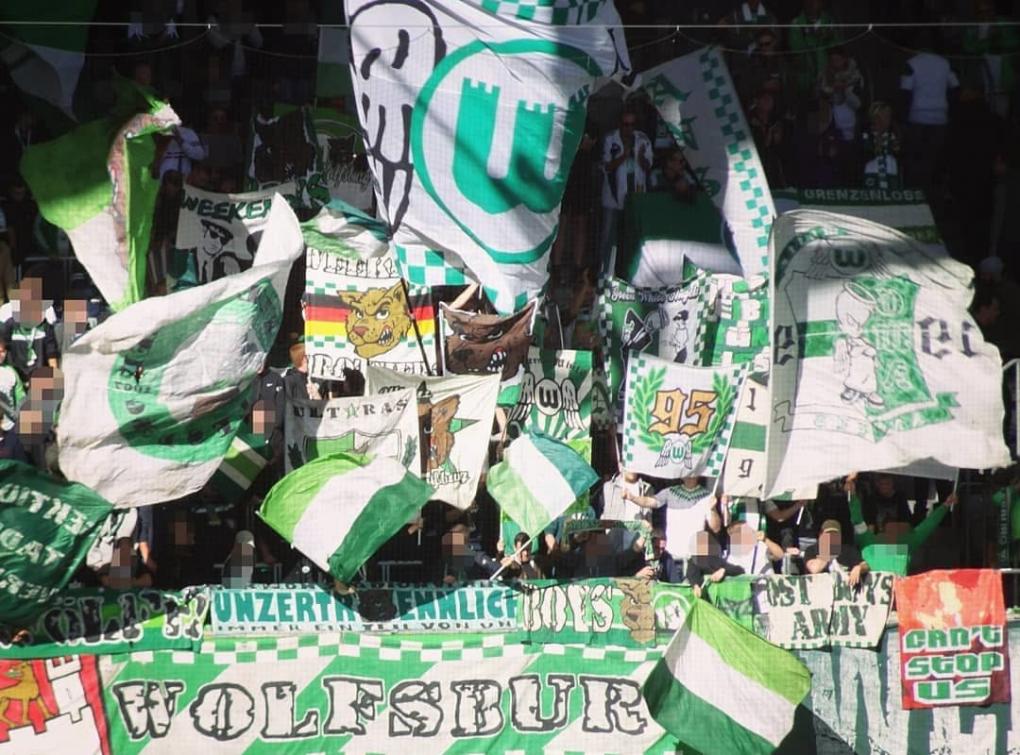 VfL Wolfsburg-Fans mit Fahnen und Doppelhaltern hinterm "Wolfsburg"-Banner