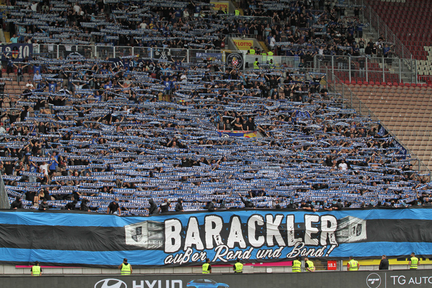 "Barackler außer Rand und Band!"-Plakat. Dahinter halten Waldhof-Fans Schals hoch.