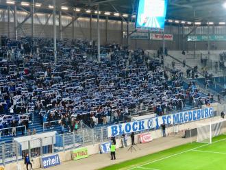 FCM-Fans halten hinter den Block U - 1. FC Magdeburg-Zaunfahnen ihre Schals hoch.
