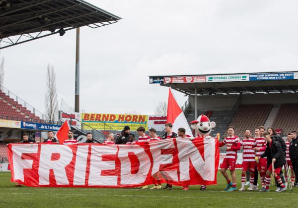 FC Energie Cottbus-Spieler mit einem "Frieden"-Plakat der eigenen Fans.