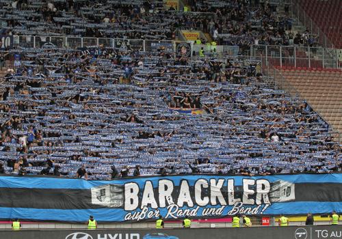 "Barackler außer Rand und Band!"-Plakat. Dahinter halten Waldhof-Fans Schals hoch.