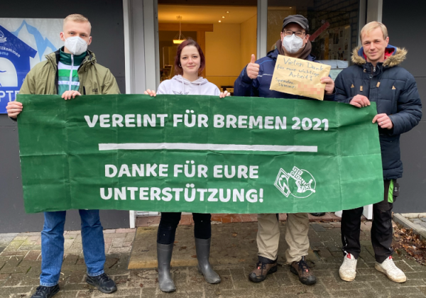 Spendenübergabe hinter "Vereint für Bremen 2021"-Banner.