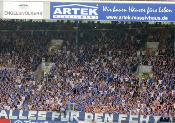Hansa-Fans am 27.07.2021 mit ausgestreckten Händen auf der vollen Südtribüne Rostock.