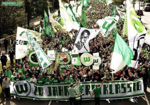 Fanmarsch von VfL Wolfsburg-Fans hinter einer "20 Jahre erstklassig"-Fahne.