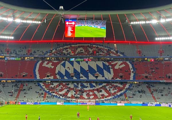 FC Bayern München-Wappen aus Sitzschalen im Stadion. Teilweise sitzen Fans auf den Sitzen.